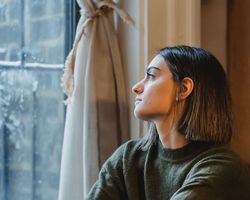 Junge, nachdenkliche Frau am Fenster: Burnout oder Erschöpfung?