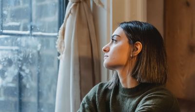 Junge, nachdenkliche Frau am Fenster: Burnout oder Erschöpfung?