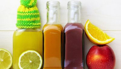 Immunsystem natürlich stärken: zu sehen sind verschiedene Säfte in Glasflaschen, Zitronenscheiben und ein Apfel. Auf einem Flaschenhals sitzt eine kleine Mütze